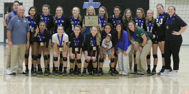 group of volleyball players and coaches posing in gym in front of volleyball net