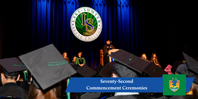 Wide-angle view from the audience at a Lake-Sumter State College commencement, showing graduates in black caps facing a stage with administrators and speakers beneath a large illuminated college seal, with a blue banner at the bottom reading “Seventy-Second Commencement Ceremonies” alongside the college crest.