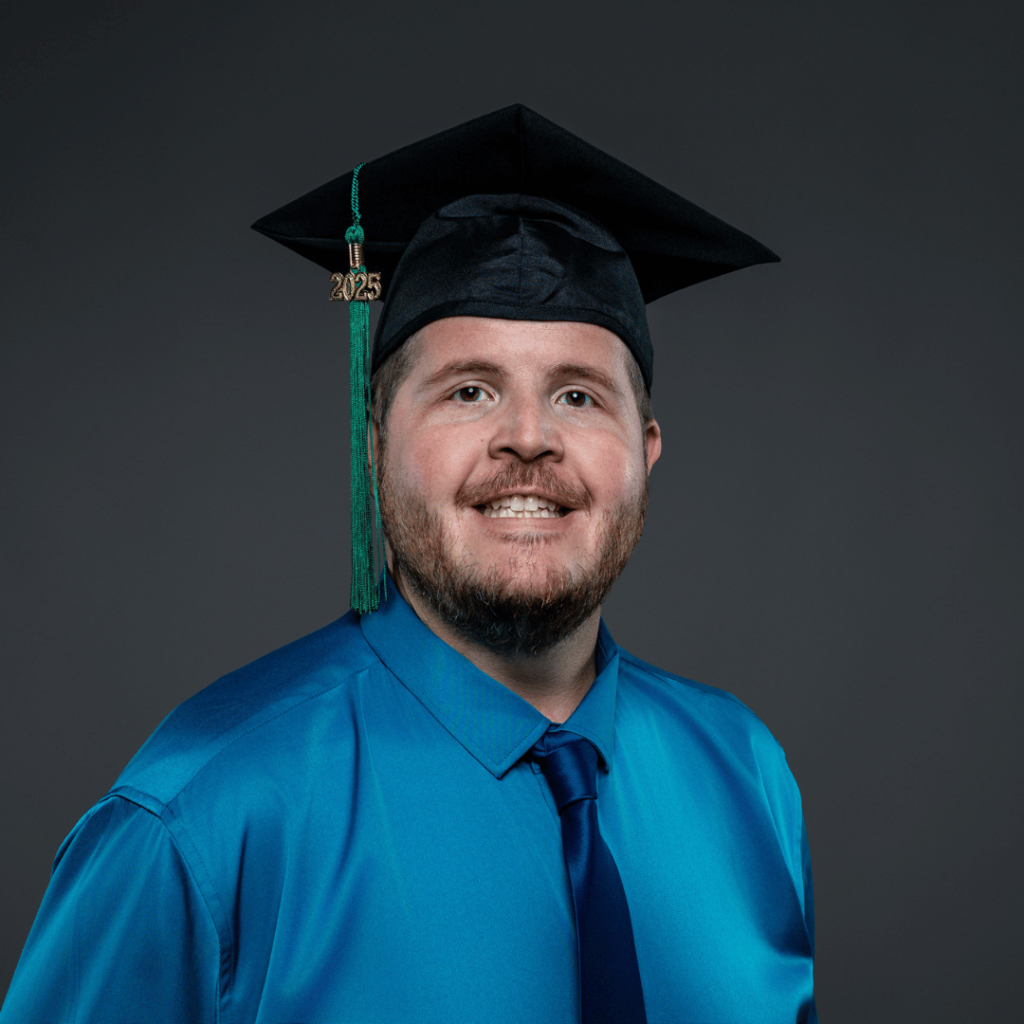 Graduate in a teal dress shirt and dark tie stands against a dark gray background, wearing a black cap with a green tassel and gold “2025” charm.