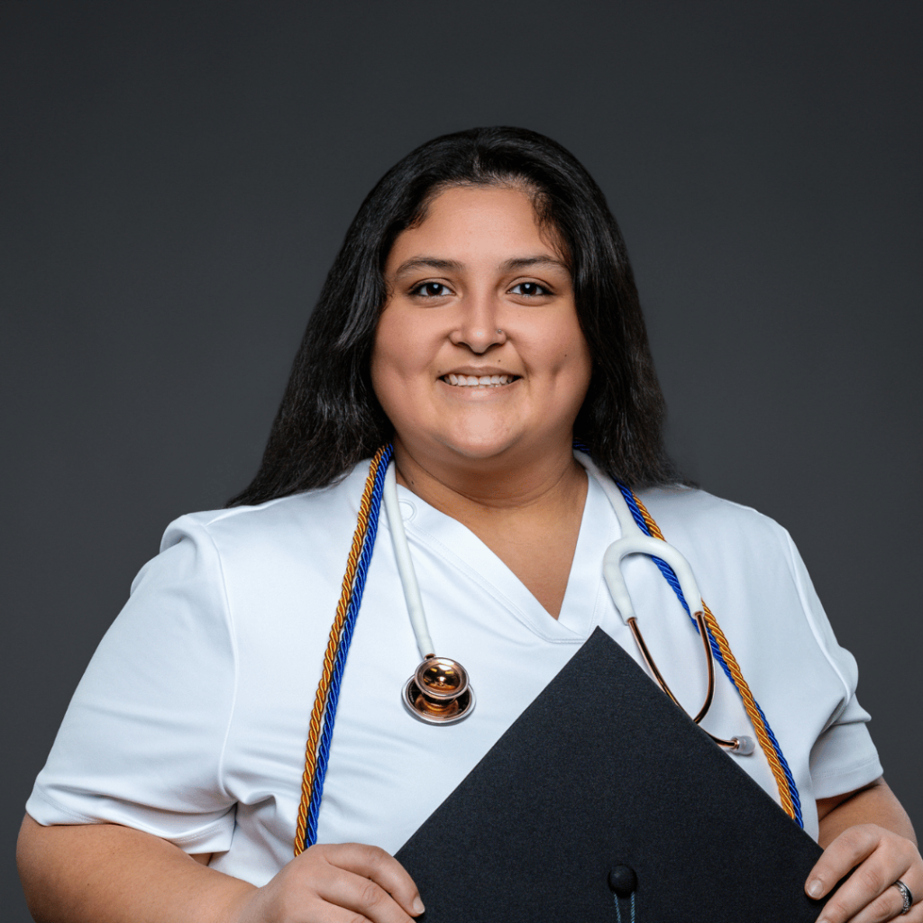 Nursing graduate with long hair poses in a black cap and gown against a dark gray background, wearing a stethoscope and a cap with a green tassel and gold “2025” charm.