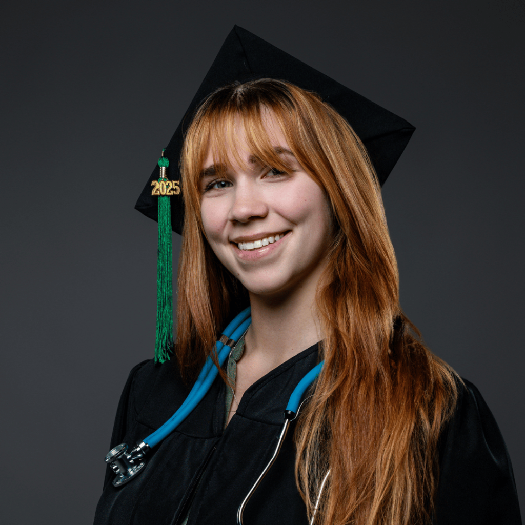 Nursing graduate with long hair poses in a black cap and gown against a dark gray background, wearing a stethoscope and a cap with a green tassel and gold “2025” charm.