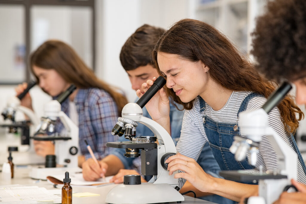 young student looking in a microscope among other students