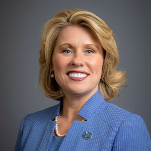 Portrait photo of President Heather Bigard smiling in a blue suit with a gray background