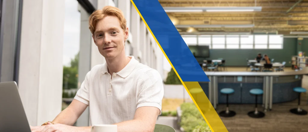 Red haired male student completing work on laptop
