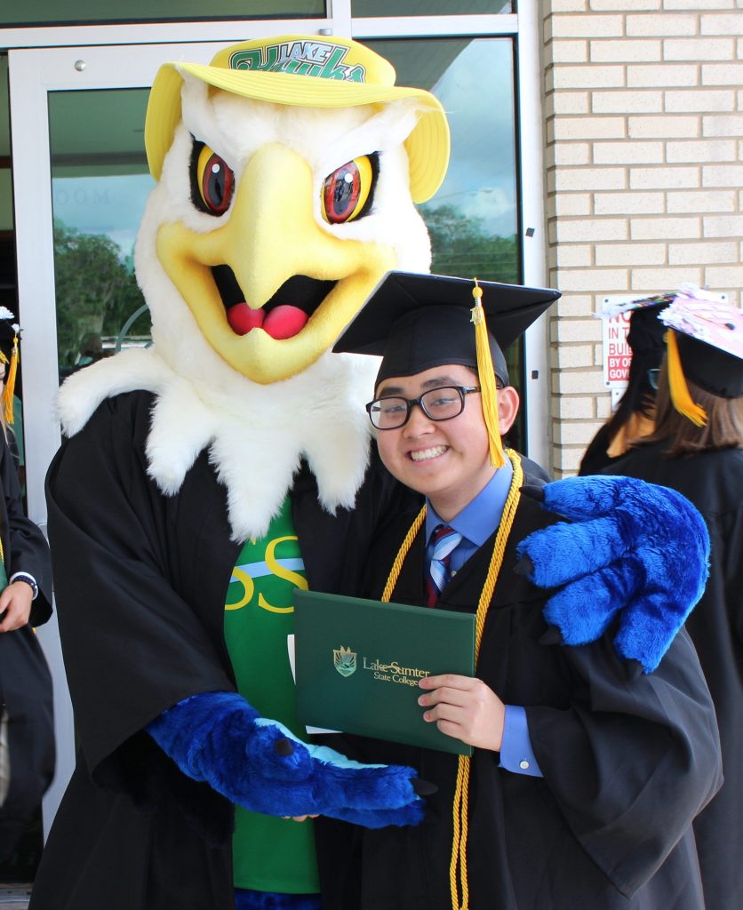 Mascot swoop with a LSSC graduate holding a diploma both wearing a cap and gown