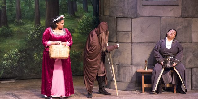 2 characters dresses in medieval attire on stage with forest and castle as background