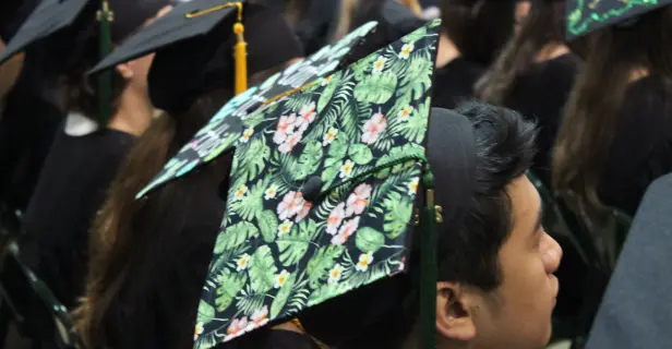 Student wearing graduation cap with green tropical leaf and hibiscus pattern.