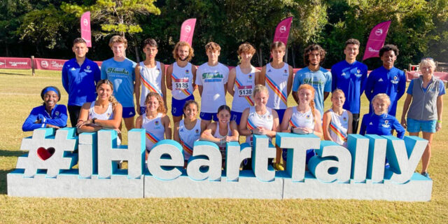 cross country runners stand lined up in front of big lettering I heart Tally