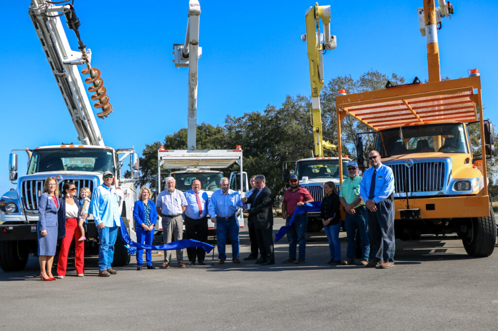 People line up for a ribbon cutting in front of large trucks with buckets raised