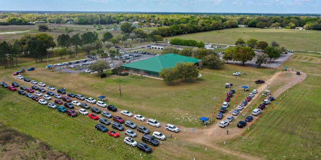 Car lines up in the grass around building at Sumter Center for COVID-19 vaccination