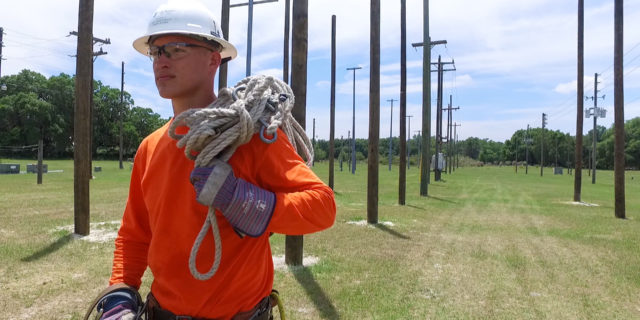 Man walking near utility poles with a hard hat and gear