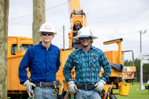 Two lineworker students pose for a photo in front of a yellow utility truck