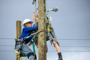 Lineworker student performs a pole top rescue with weighted mannequin