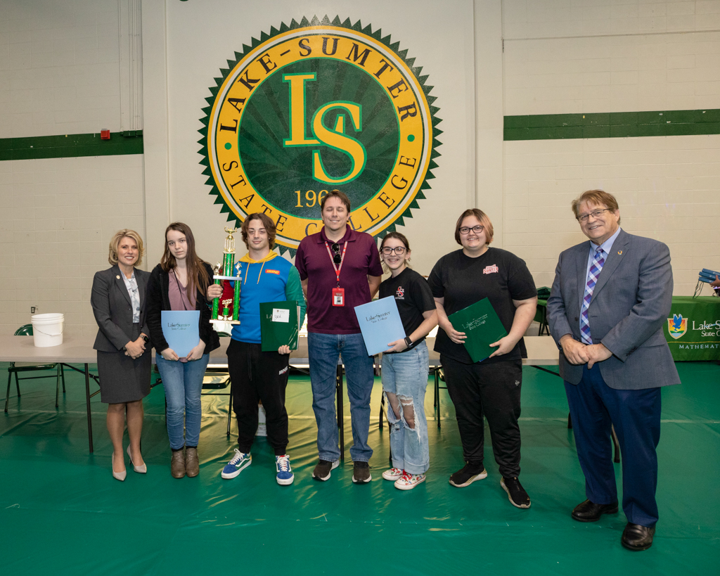 students and faculty standing in line for a photo holding a trophy