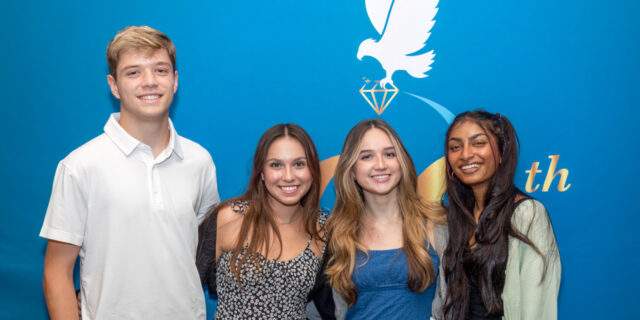 Four people standing in front of a blue backdrop smiling
