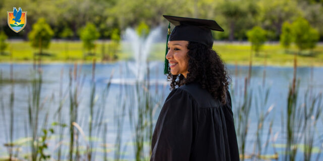 A student smiles while wearing a black graduation cap and gown