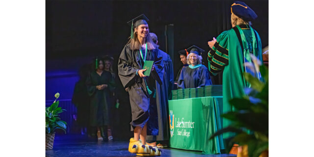 Makenzi Heaton walks across the stage at commencement donning her Swoop feet, revealing herself as the mascot