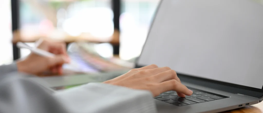Close-up of individual typing on laptop with one hand, writing on accessible canvas pages with the other, setting unclear.
