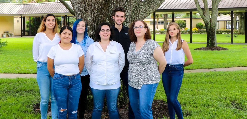 group of students posing outside in front of tree wearing white and black blouses, and blue jeans