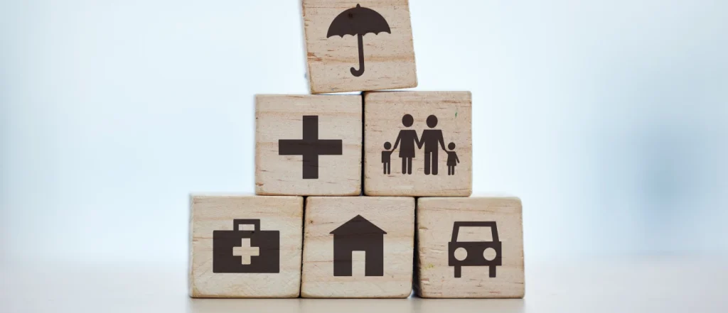 Wooden blocks stacked in a pyramid, depicting a plus sign, a family of four, a medical symbol, a house, and a car.