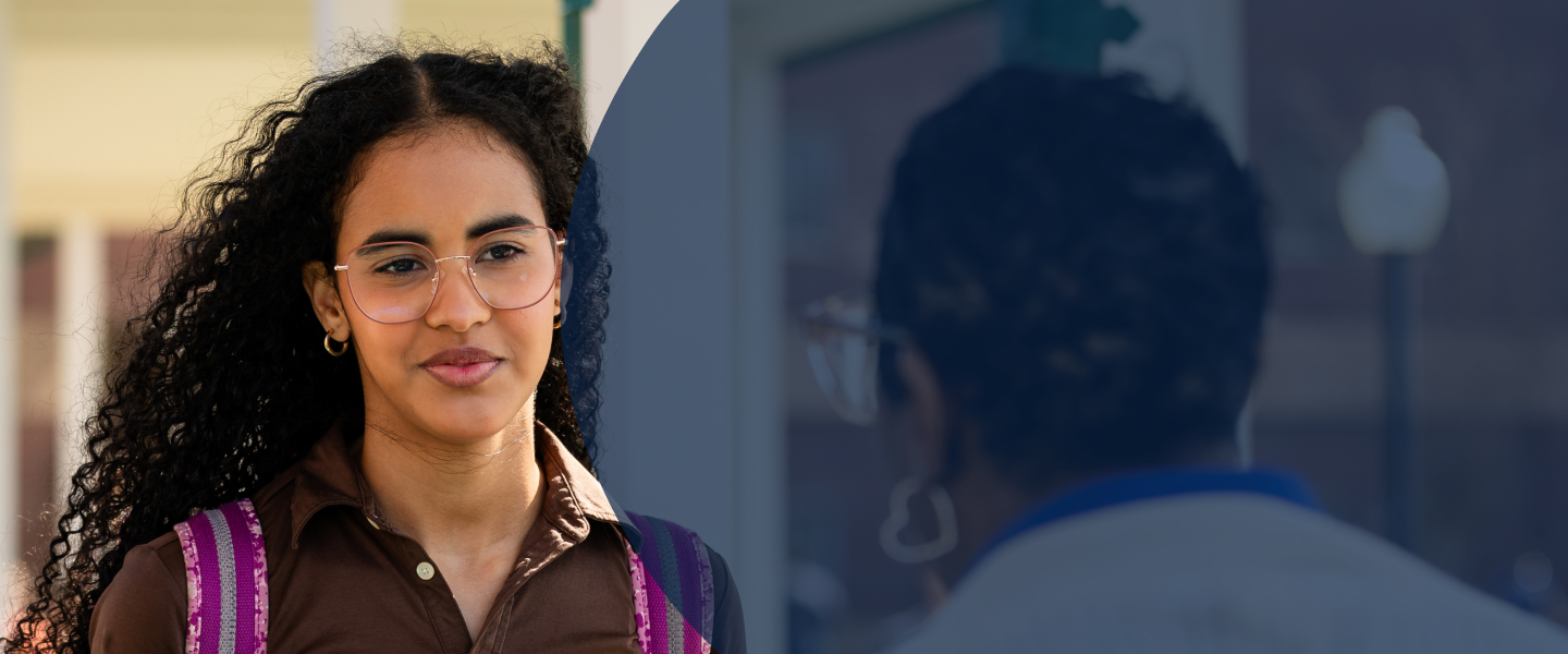 Person with curly hair, glasses, brown shirt, pink backpack stands outdoors facing another individual.