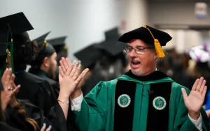 Instructor in regalia high-fives students in graduation attire at ceremony setting.