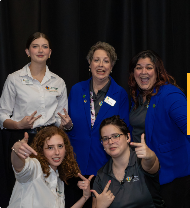 Events team and student workers pose and smile in front of a black curtain; some make playful hand gestures toward the camera.