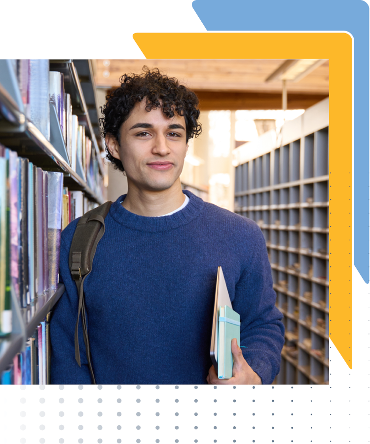 Student with curly hair smiling, holding books, standing between library bookshelves, representing leadership development.