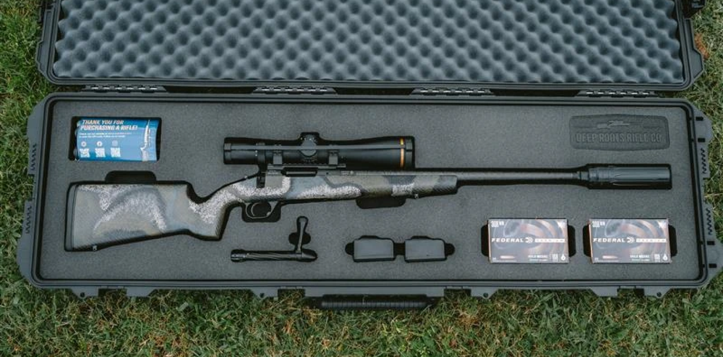 Scoped rifle in foam-lined hard case with ammo boxes, accessories on grass.