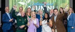 Group of people with awards posing on stage by Distinguished Alumni sign, event setting.