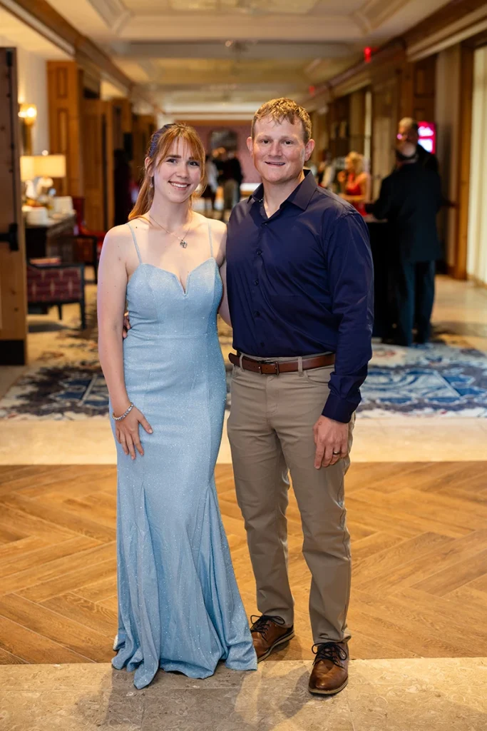 Dolan Waite and his wife pose together in warmly lit indoor setting, wearing semi-formal attire.