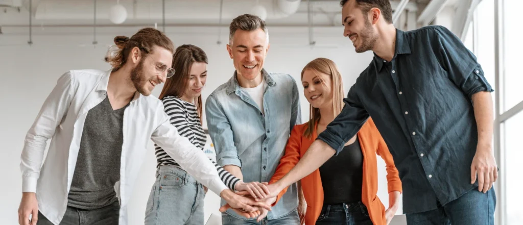 Five young adults stand in a line, arms raised, forming a human pyramid with one person at the top.