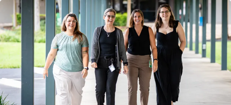 Four individuals walking outdoors under covered walkway, smiling and appearing relaxed. No visible role indicators.