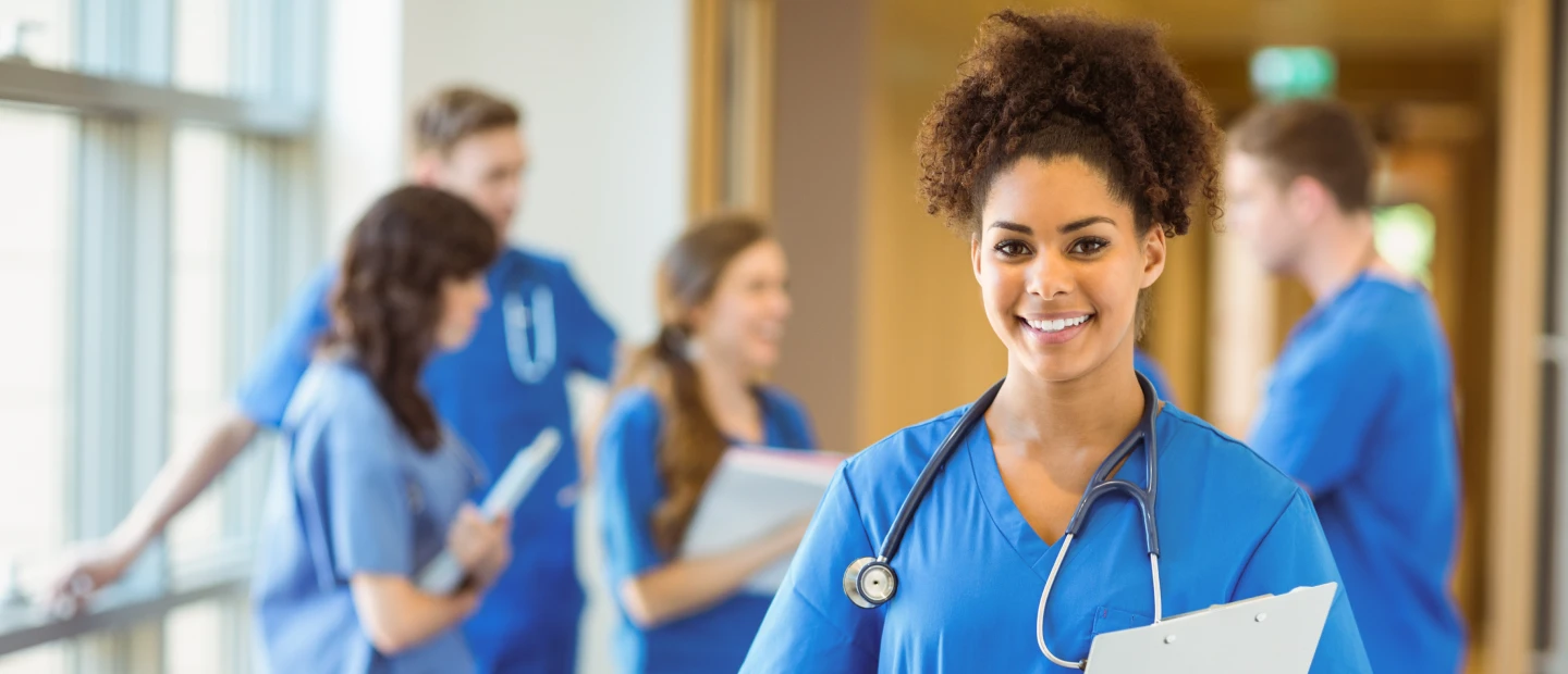 1 image files updated Smiling nurse in scrubs stands in a hospital hallway with colleagues in the background