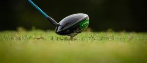 Golf club head near golf ball on grass, preparing for shot; blurred course background.