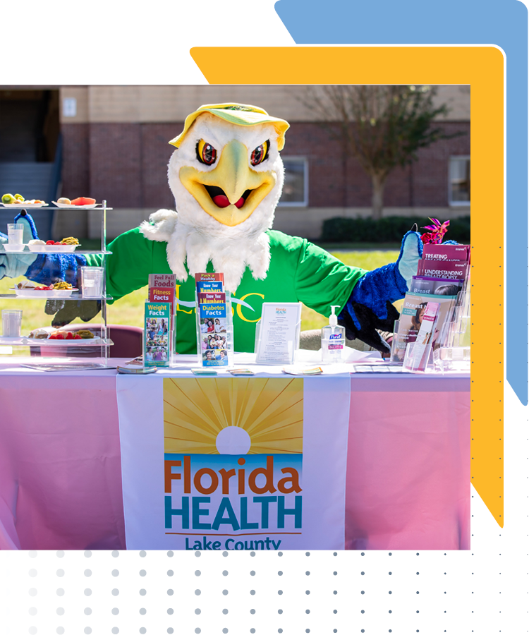 Swoop, LSSC mascot, is sitting behind a Florida Health table at a Employee Health Benefit Fair