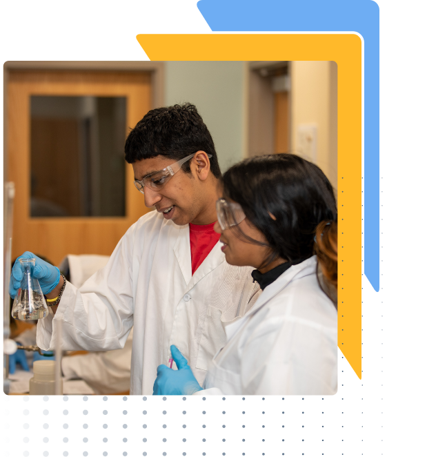 Two individuals in lab coats and gloves hold a flask in a laboratory, wooden door visible in background.