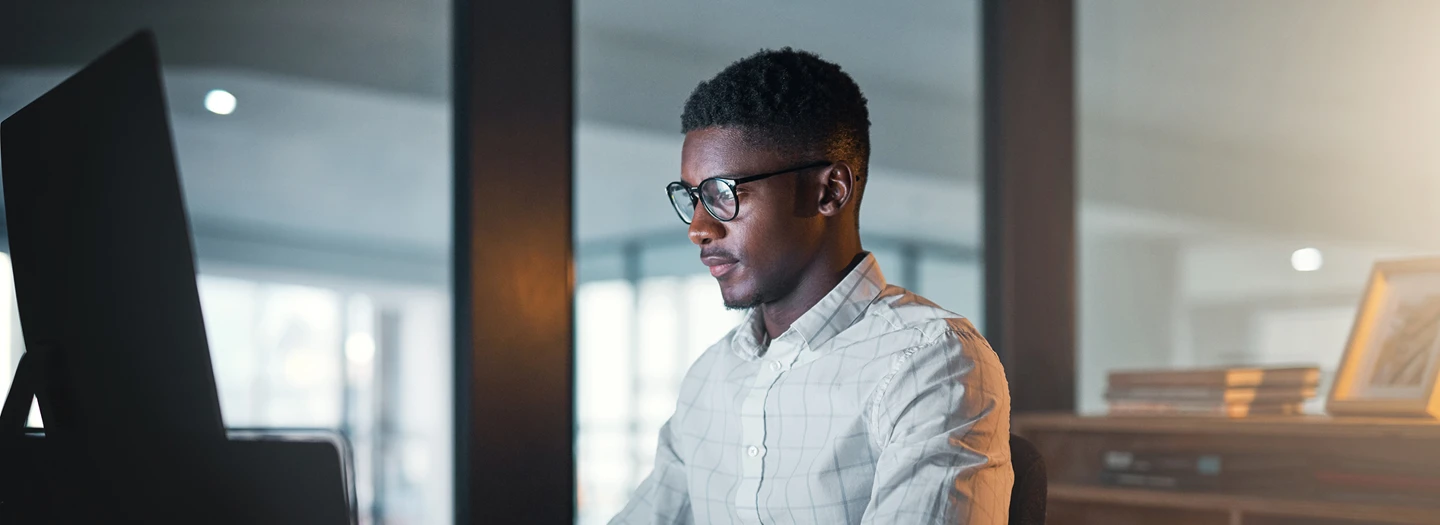 Person sitting at a desk working on a computer, behind them are large windows and shelves holding books and picture frames