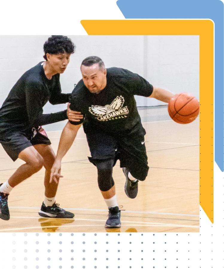 Dr. Mews, and student playing basketball indoors; Dr. Mews, dribbles the ball while the student defends closely.