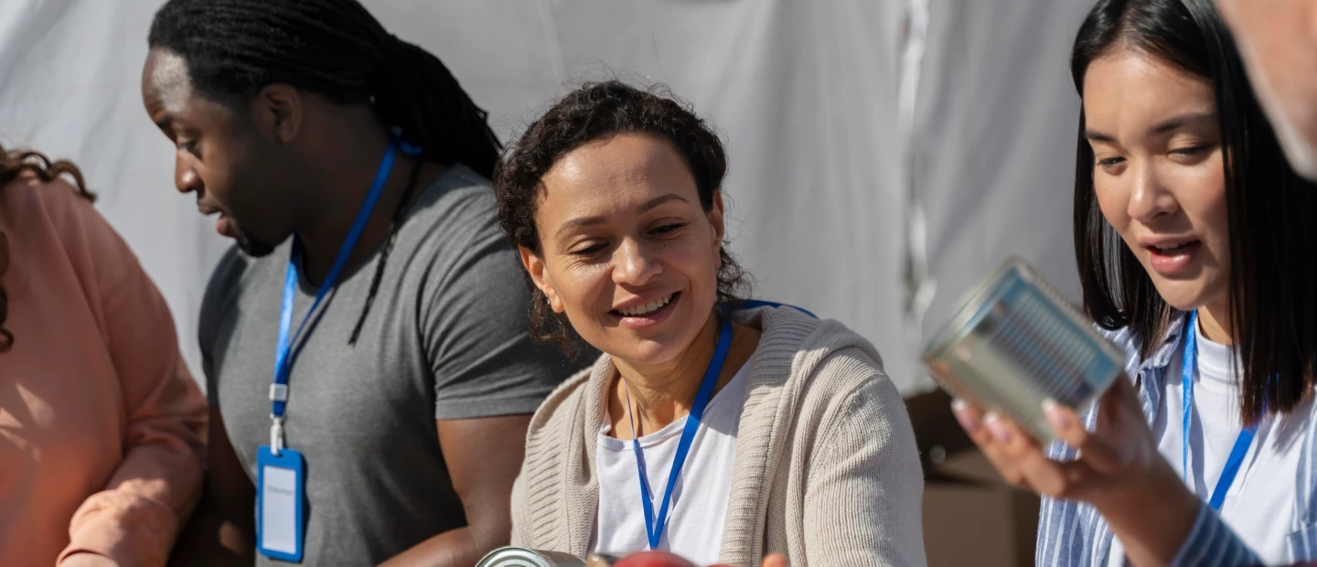 group of people with blue lanyards and name tags stand under a white canopy, with canned goods visible in the foreground