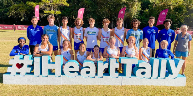 Group of individuals in athletic gear posing behind a large #IHeartTally sign on a grassy field.