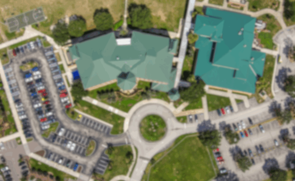 Aerial view, blurred campus, green-roofed buildings, parking lots, circular driveway near Student Assistance Program.