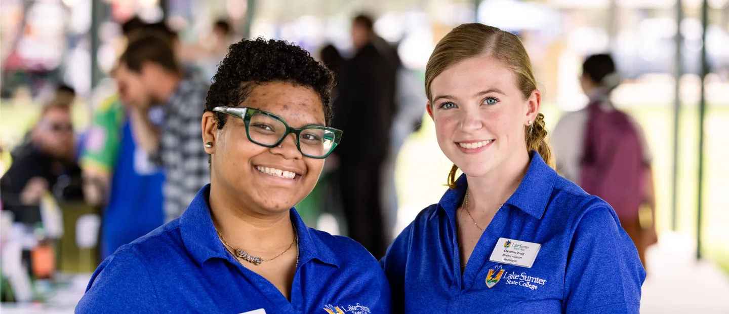 Two staff with badges in blue Lake-Sumter State College polo shirts smiling at an event.