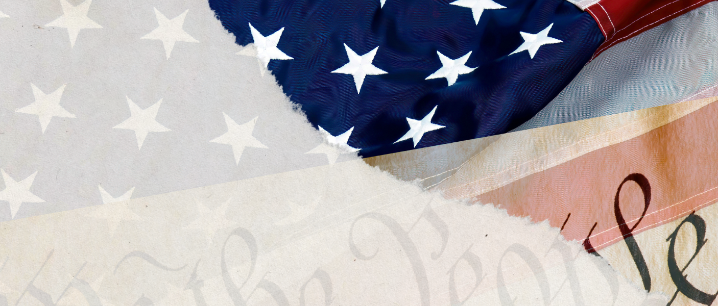 Folded American flag overlaps faded U.S. Constitution, partial “We the People” text visible, close-up view.